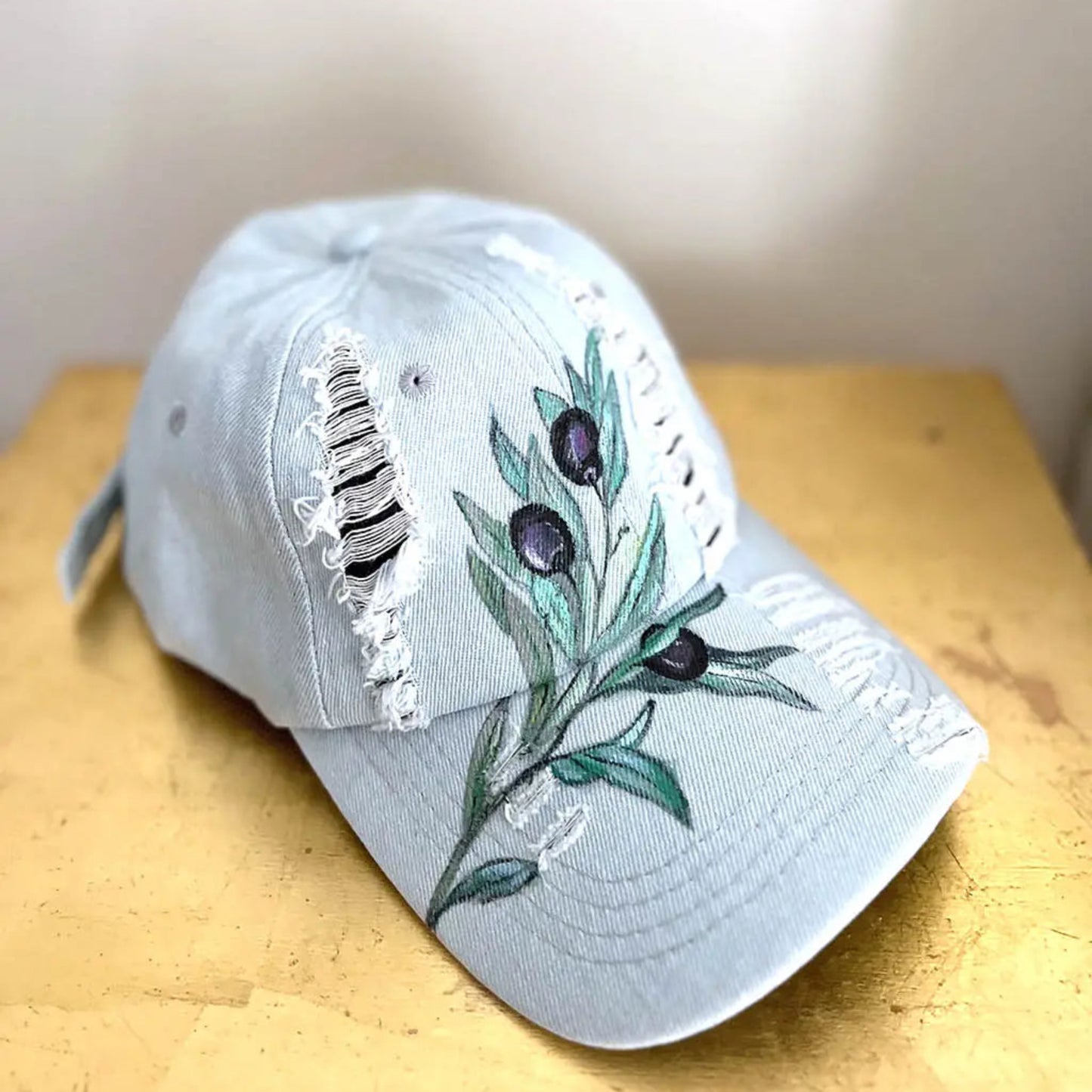  blue/gray wash ripped denim baseball cap with an olive branch and three olives hand-painted on the front.
