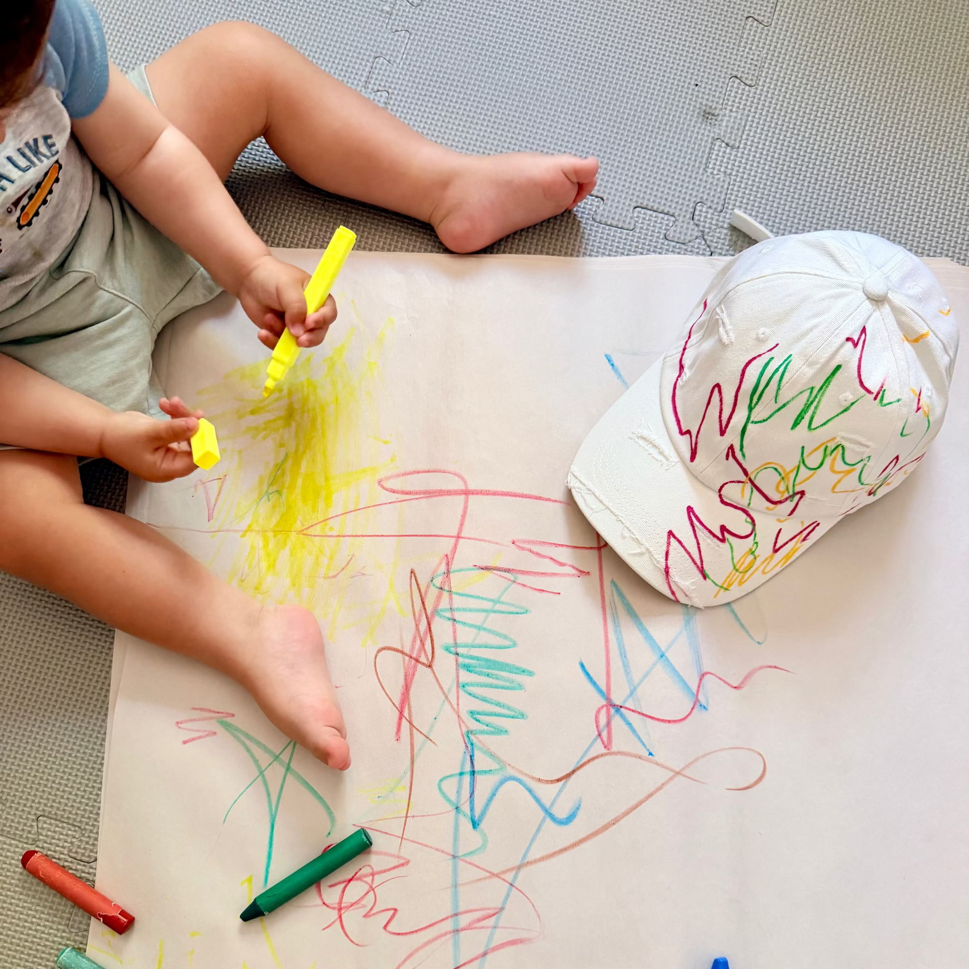 Child drawing on a large piece of paper with crayons, wearing a hard hat.