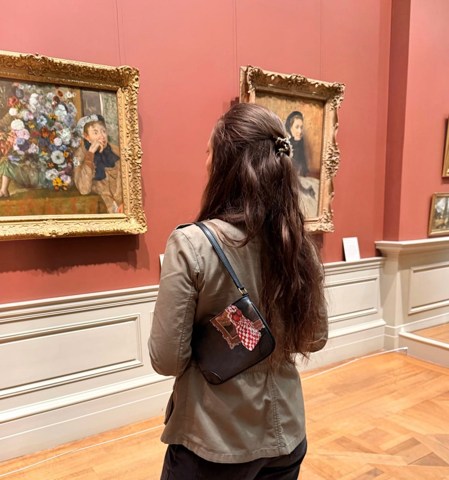 Woman looking at paintings in an art gallery with a red wall, wearing a handprinted jacket that features a still life painting with apples.