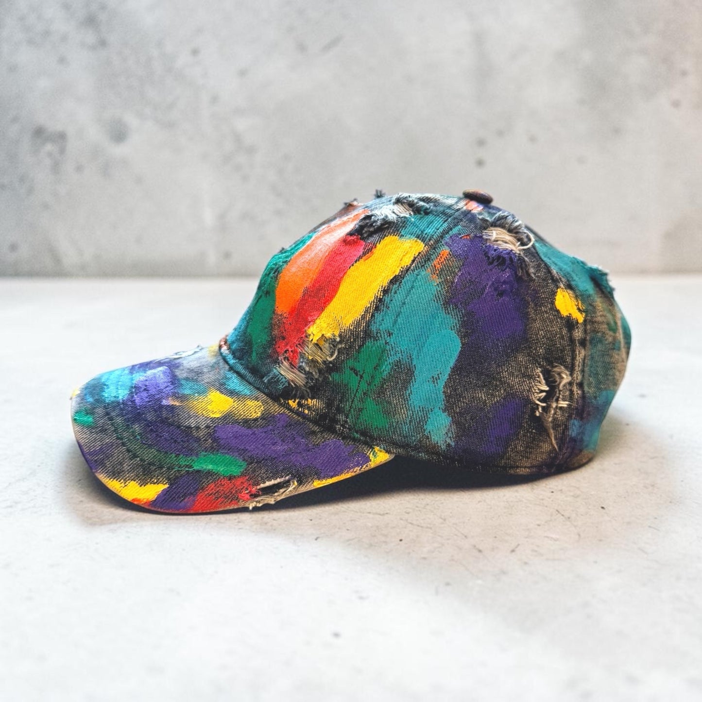 Colorful paint-splattered cap on a concrete surface with a gray background