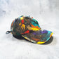 Colorful distressed baseball cap with 'Rebelle Theory' branding on a gray surface