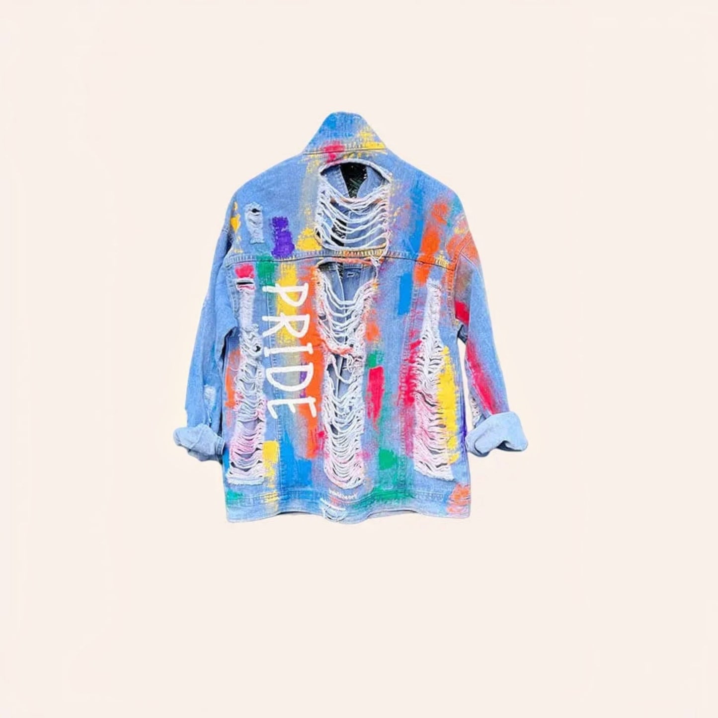 A light blue distressed denim jacket featuring colorful abstract paint splatters and the word 'PRIDE' printed vertically in white on the front, set against a solid pale beige background.