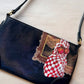 Black handbag with a decorative patch featuring a hand painted  checkered fabric and apples on a light background