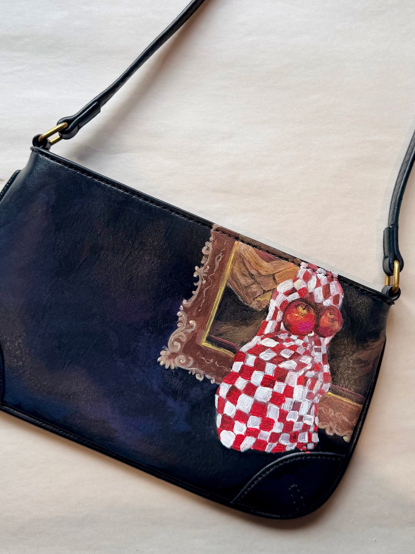 Black handbag with a decorative patch featuring a hand painted  checkered fabric and apples on a light background