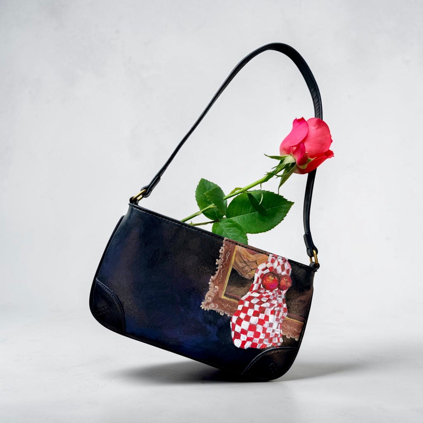 Black handbag with a red rose and decorative elements featuring hand painted still life with apples on a light gray background