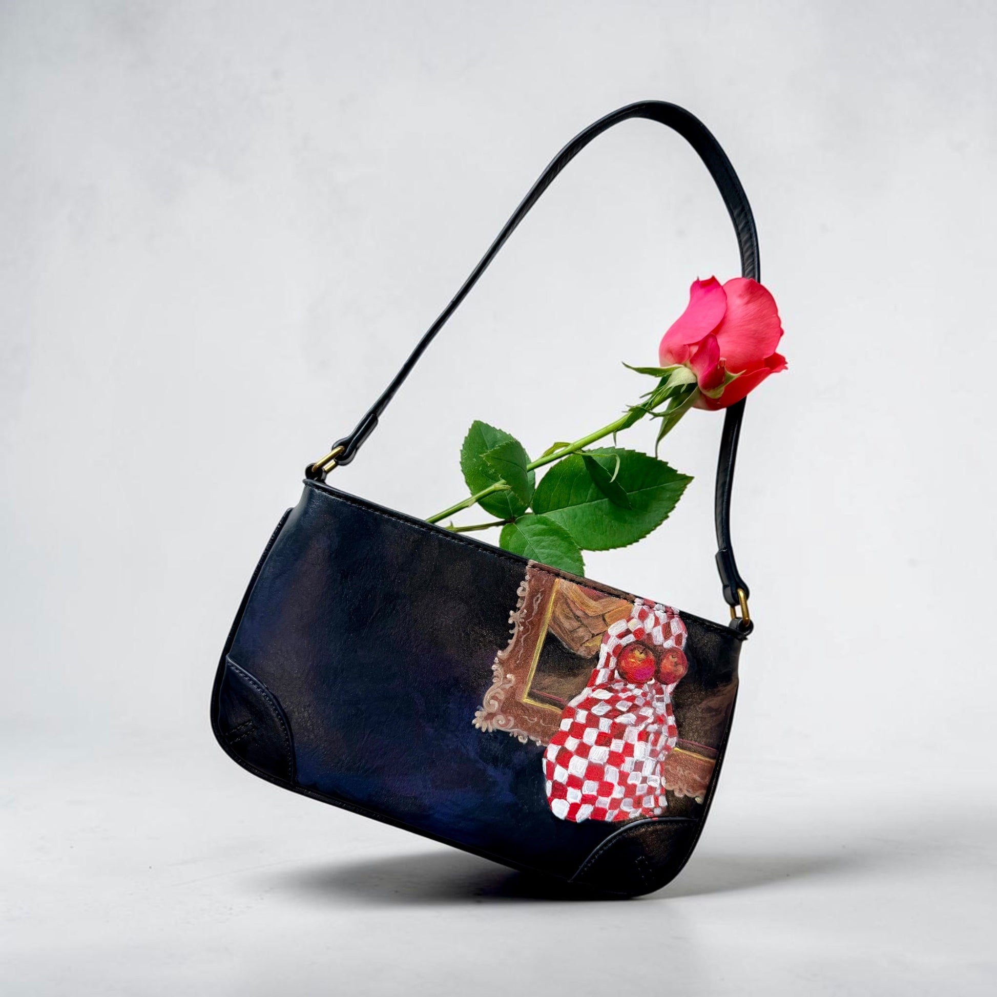 Black handbag with a red rose and decorative elements featuring hand painted still life with apples on a light gray background
